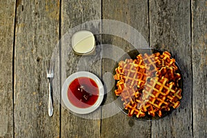Top view of curd waffles on a plate, apricot jam, a glass of milk and a fork on a wooden table
