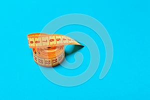 Top view of curled measuring tape as a sewing accessory on blue background. Tailor concept with copy space