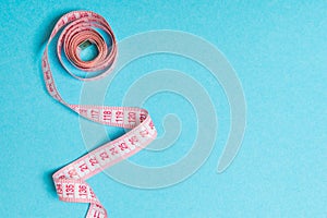 Top view of curled measuring tape as a sewing accessory on blue background. Tailor concept with copy space