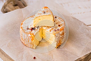 Top view of cut slice of French or German soft cheese with orange rind with mold, creamy texture, red pepper corns