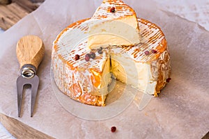 Top view of cut slice of French or German soft cheese with orange rind with mold, creamy texture, red pepper corns, fork