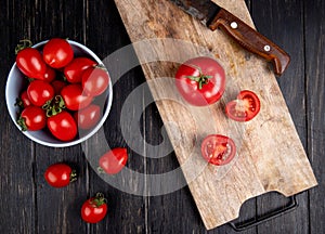 top view of cut and whole tomatoes and knife on cutting board with other ones in bowl on wooden background