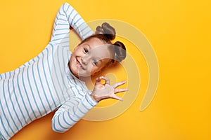 Top view of a cute adorable little girl with bundles of hair on a yellow background. The child shows the sign ok. Close up copy
