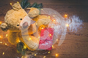 View of a teddy with a red wrapped present, and Christmas decorations on wooden background