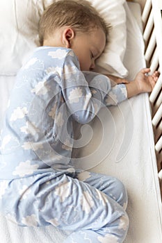 top view Cute little 2-3 years preschool baby boy kid sleeping sweetly in white crib during lunch rest time in blue