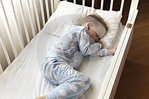 Top view Cute little 2-3 years preschool baby boy kid sleeping sweetly in white crib during lunch rest time in blue pajama with