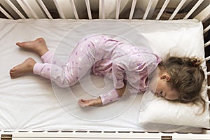 top view Cute little 3-4 years preschool baby girl kid sleeping sweetly in white crib during lunch rest time in pink