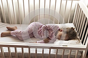 top view Cute little 3-4 years preschool baby girl kid sleeping sweetly in white crib during lunch rest time in pink