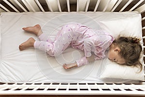 Top view Cute little 3-4 years preschool baby girl kid sleeping sweetly in white crib during lunch rest time in pink pajama with