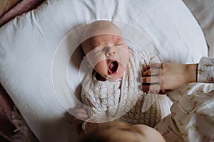 Top view of cute little baby yawning in bed, big sister holding newborn hand. Sisterly love, joy for new family member.