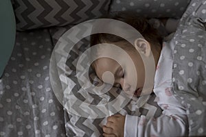 top view Cute little chubby baby girl kid sleeping sweetly in grey crib during lunch rest time in white and pink pajamas