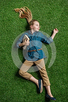 Top view of cute little girl with book lying on green grass