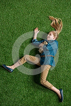 Top view of cute little girl with book lying on green grass