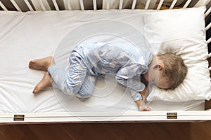 top view Cute little 2-3 years preschool baby boy kid sleeping sweetly in white crib during lunch rest time in blue