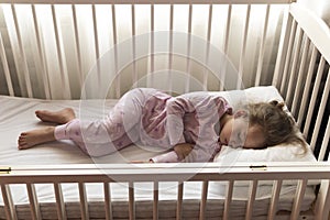 Top view Cute little 3-4 years preschool baby girl kid sleeping sweetly in white crib during lunch rest time in pink pajama with