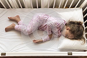 top view Cute little 3-4 years preschool baby girl kid sleeping sweetly in white crib during lunch rest time in pink