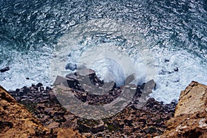 Top view of dangerous rocky beach seashore coastline surrounded by stormy waves, steep cliffs, stones, boulders cobbles.