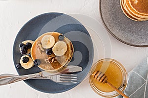 Top view of a dark ceramic plate with pancakes, with nuts and slices of fresh banana to enhance the taste. a bowl of honey.