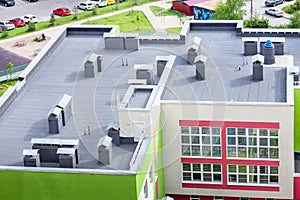 Top view dark flat roof with air conditioners and hydro insulation membranes modern school building residential area.