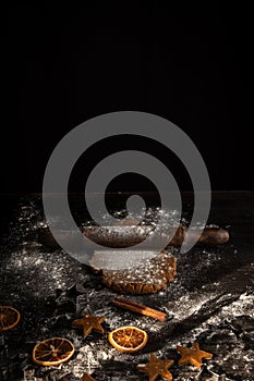 Top view of dark table with gingerbread cookie dough with rolling pin, flour and molds, black background,