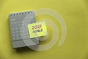 Top view of december 2020 calendar with sticky note written with 2021 Goals on yellow background with copy space