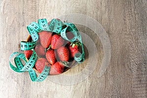 Top view of delicious big red strawberry in round wooden plate covered by measuring tape