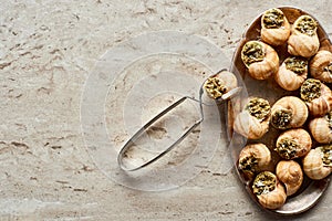 Top view of delicious cooked escargots on plate with tweezers on stone background.