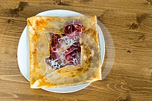 Top view of delicious crepe with dried meat pastrami served on a white plate