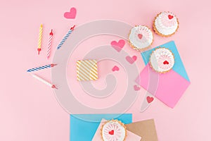 Top view of delicious cupcakes, colorful candles and hearts symbols on pink