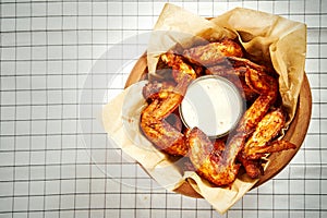 Top view of delicious fried chicken wings in a bowl, fries on a checkered tablecloth