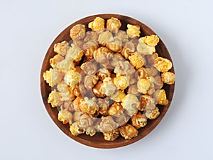 Top view of delicious popcorn in round wooden plate isolated on white background.