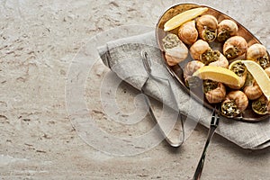 Top view of delicious served escargots with lemon on stone background.