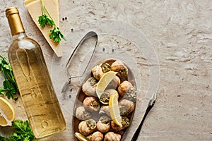 Top view of delicious served escargots near bottle of white wine and parmesan on stone background.