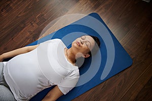 Top view of a delightful pregnant woman lying on a blue yoga mat during prenatal relaxation exercises at home
