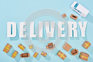 Top view of delivery lettering with shadows near cardboard boxes and van on blue background.