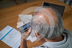 Top view of Depressed Senior Elderly male hold credit card, feel worry about financial problem. Stressed old man look to paperwork