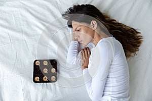 Top view depressed woman with chocolate sweets lying in bed