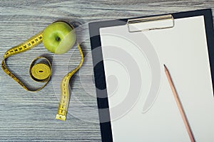 Top view on desktop with green apple and tape measure, clipboard