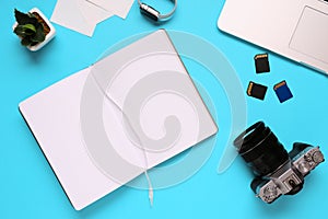 Top view of a desktop of a photographer consisting on a camera, a laptop, a notebook and a memory card on a blue desk background -