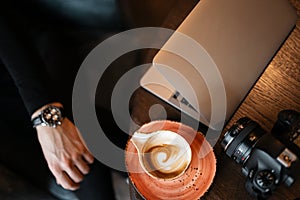 Top view of the desktop on which there is a cup of coffee, a laptop and a modern professional camera.