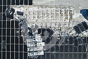 Top view of destroyed by hurricane Ian photovoltaic solar panels mounted on industrial building roof for producing green