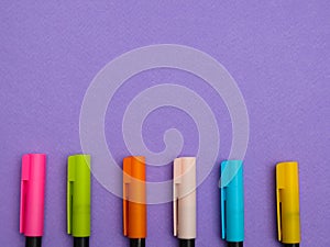 Top view of different colorfull pens or markers isolated on purple paper background