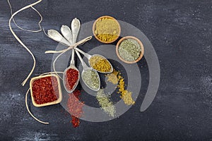 Top view of different kinds of colorful spices in spoons on black stone surface. Creative food concept texture with blank copy