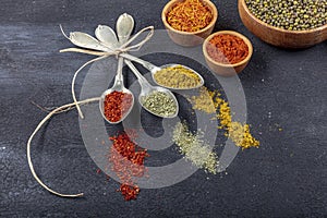 Top view of different kinds of colorful spices in spoons on black stone surface. Creative food concept texture with blank copy