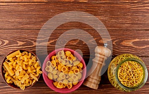 top view of different types of macaronis in bowls and salt on wooden background with copy space