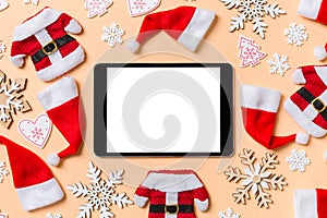 Top view of digital tablet with Christmas decorations and Santa hats on orange background. Happy holiday concept