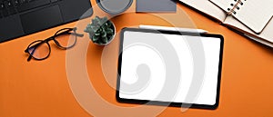 Top view of digital tablet with lank screen, stylus pen, glasses, notebook and plant  on orange background.