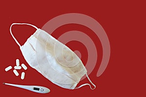 Top view of the digital thermometer, oval white tablets and face mask on red background isolated. Covid-19 pandemic concept