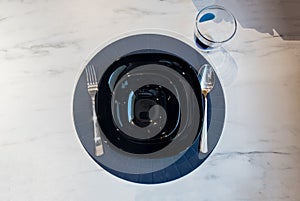 Top view of dinner place setting. A black plate with silver spoon and fork.