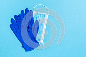 Top view of disposable medical mask and nitrile gloves on blue background. Personal protection concept with copy space